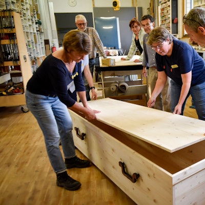 Auf dem Bild sind Teilnehmer eines Workshops mit einem selbst gebauten Holzsarg zu sehen.
