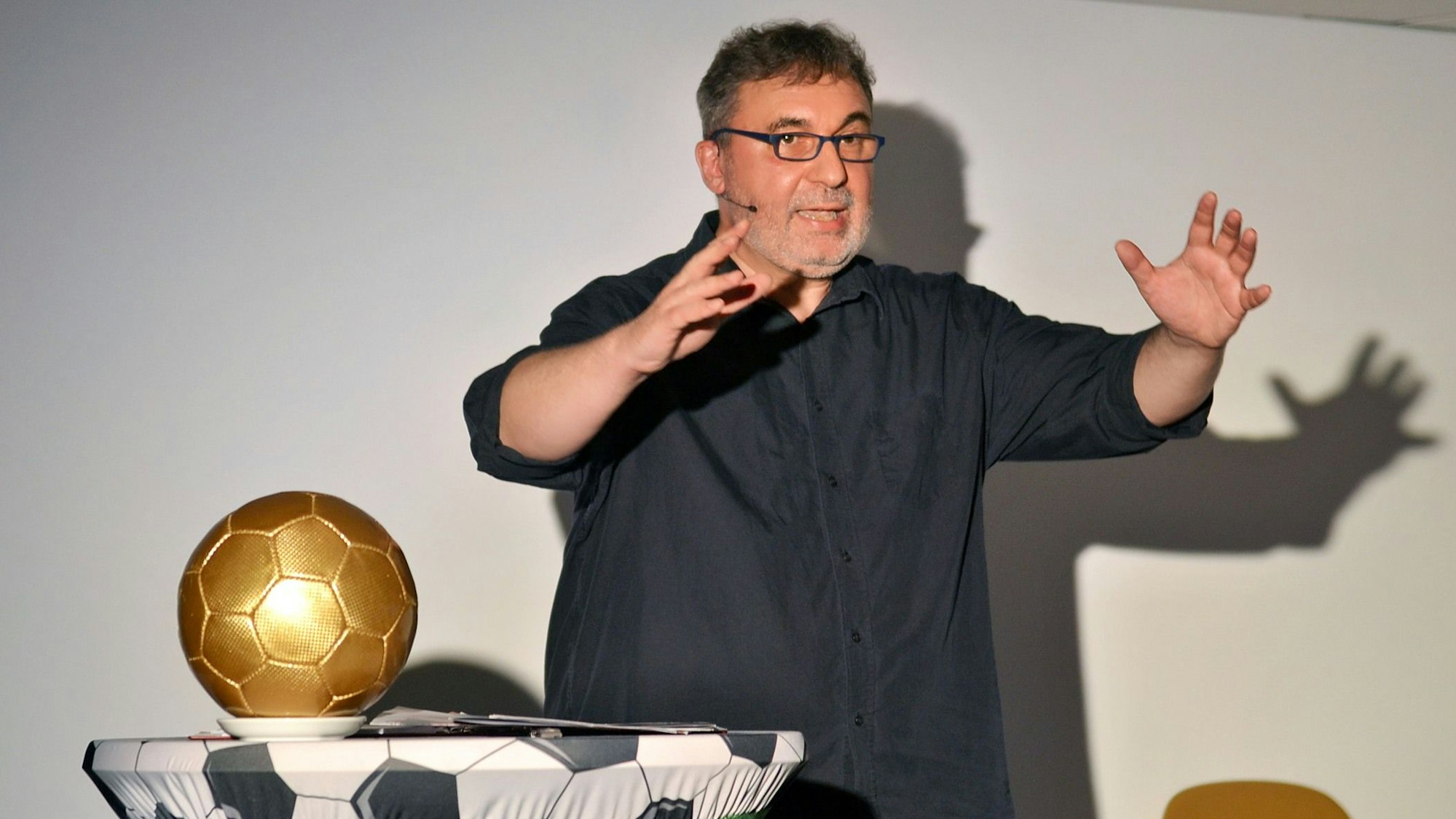 Uwe Spinder steht gestikulierend neben einem goldenen Fußball.
