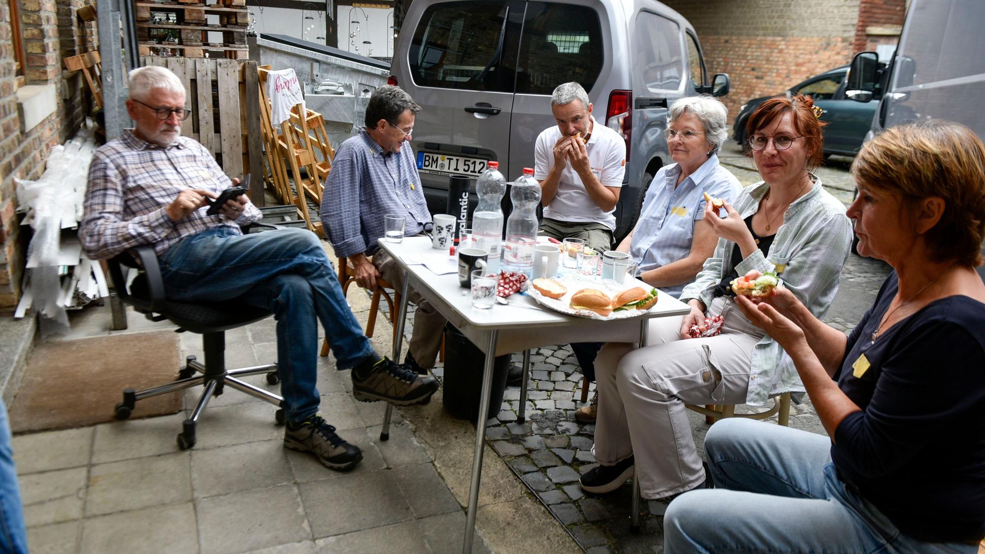 Auf dem Bild sind Menschen zu sehen, die in einem Werkstatthof sitzen und Brötchen essen.
