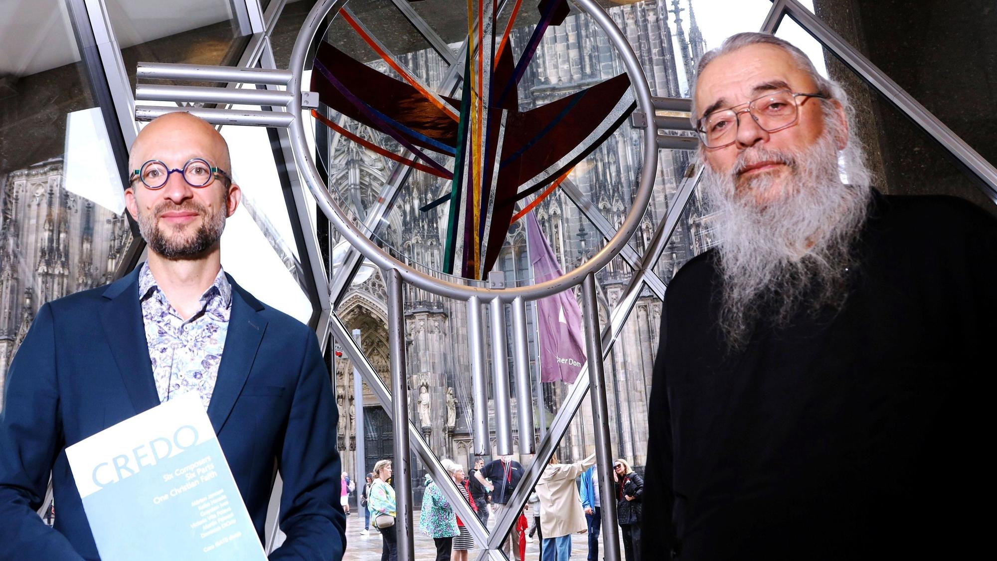 Das Bild zeigt den Kreiskantor Samuel Dobernecker (links) und den griechisch-orthodoxen Erzpriester Radu Constantin Miron zwischen dem für das Domjubiläum 1998 geschaffene Kölner Ökumene- und Versöhnungskreuz des Künstlers Rafael Seitz im Domforum. Foto: Arton Krasniqi
