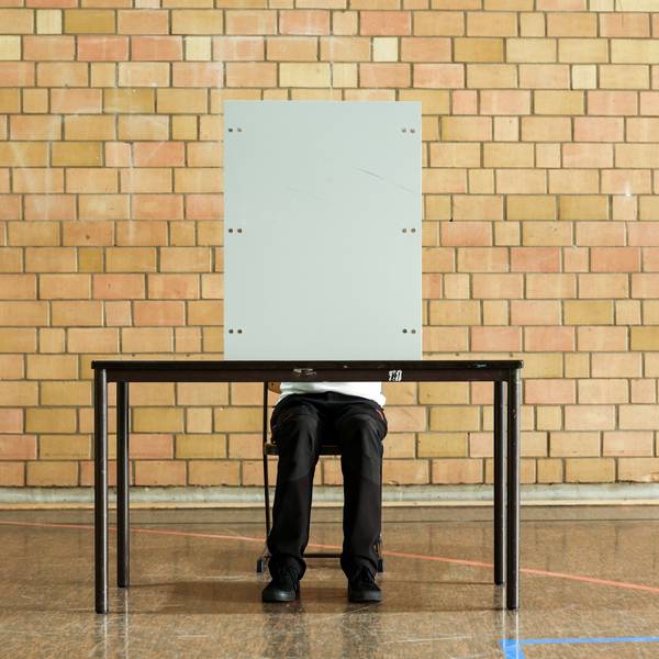 Ein Mann sitzt hinter einer Wahlkabine.