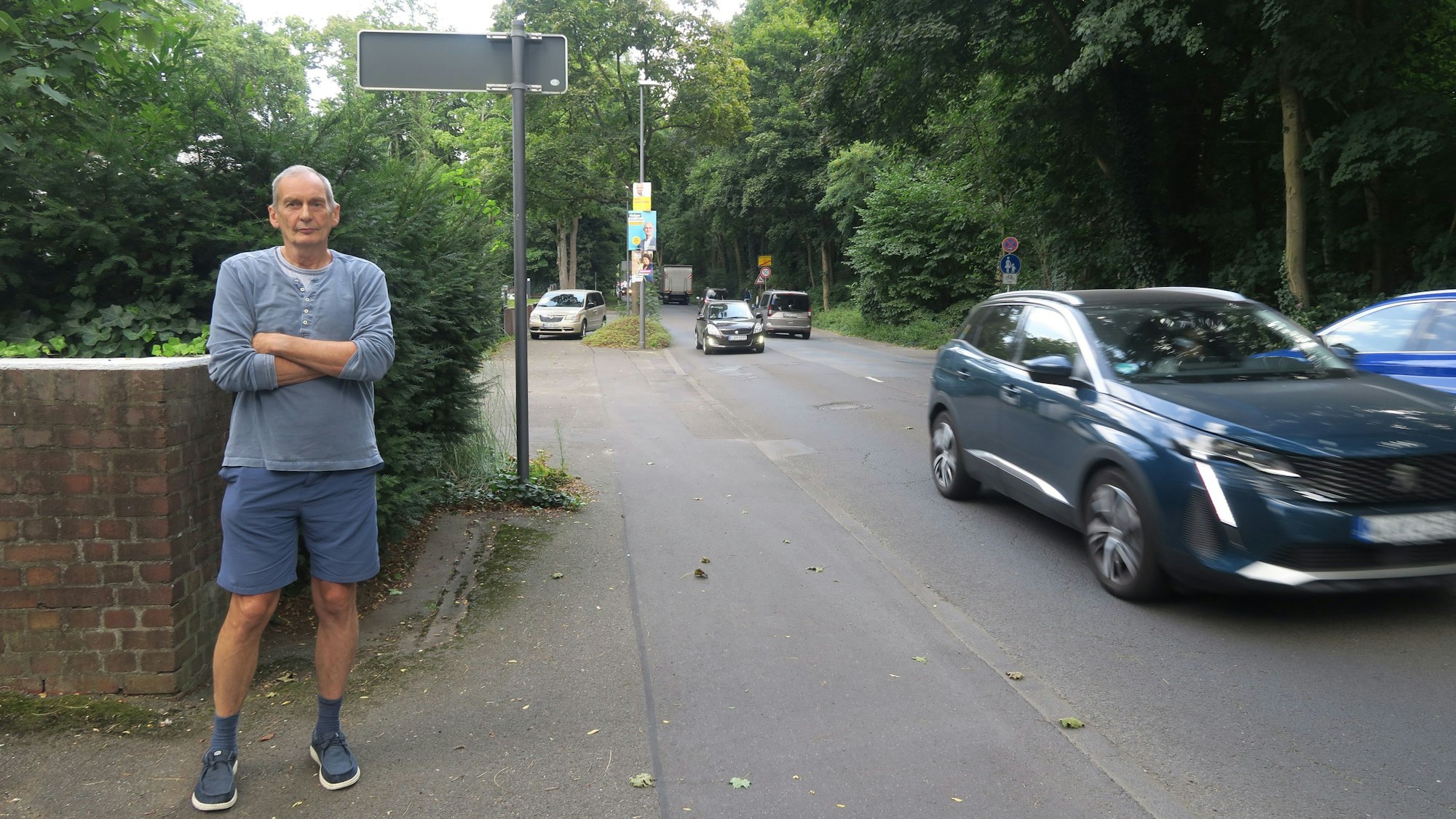 Ein Mann steht mit kurzer Hose und verschränkten Armen an einer viel befahrenen Straße.