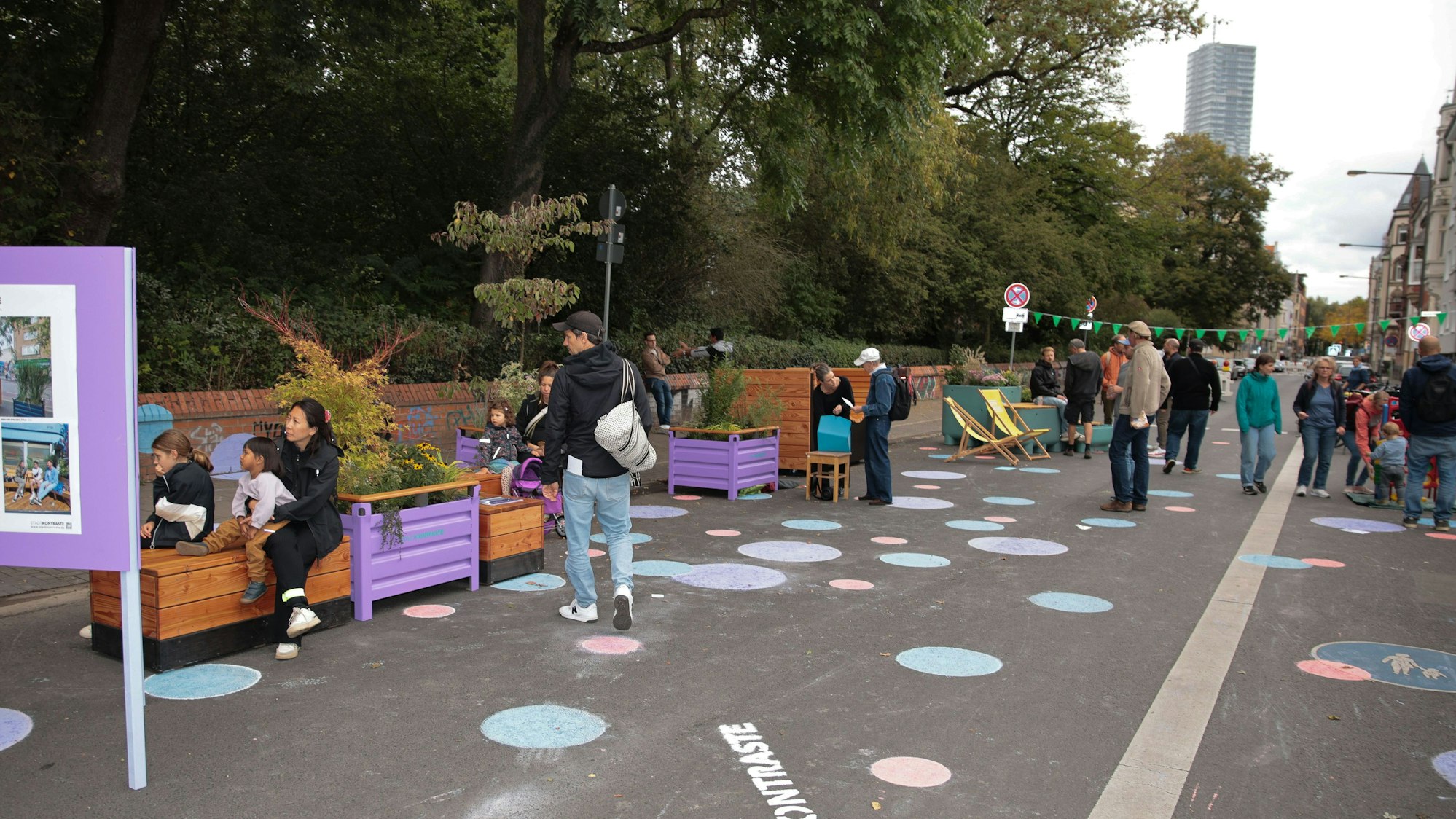 Eine Straße ist gesperrt, auf ihr stehen Sitzmöbel, sie ist mit bunten Punkten bemalt.