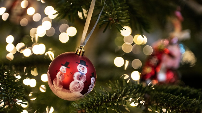 Eine Weihnachtskugel hängt an einem Weihnachtsbaum mit einer Lichterkette. (Symbolbild)