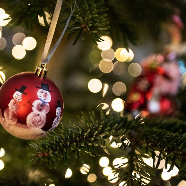 Eine Weihnachtskugel hängt an einem Weihnachtsbaum mit einer Lichterkette. (Symbolbild)