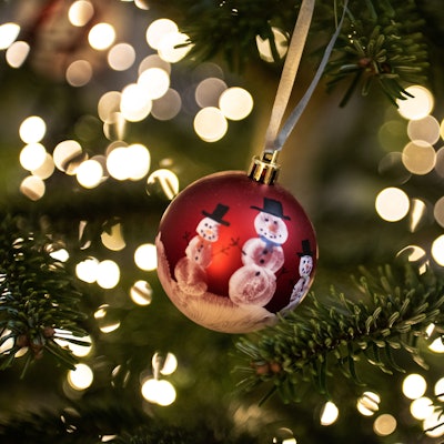 Eine Weihnachtskugel hängt an einem Weihnachtsbaum mit einer Lichterkette. (Symbolbild)