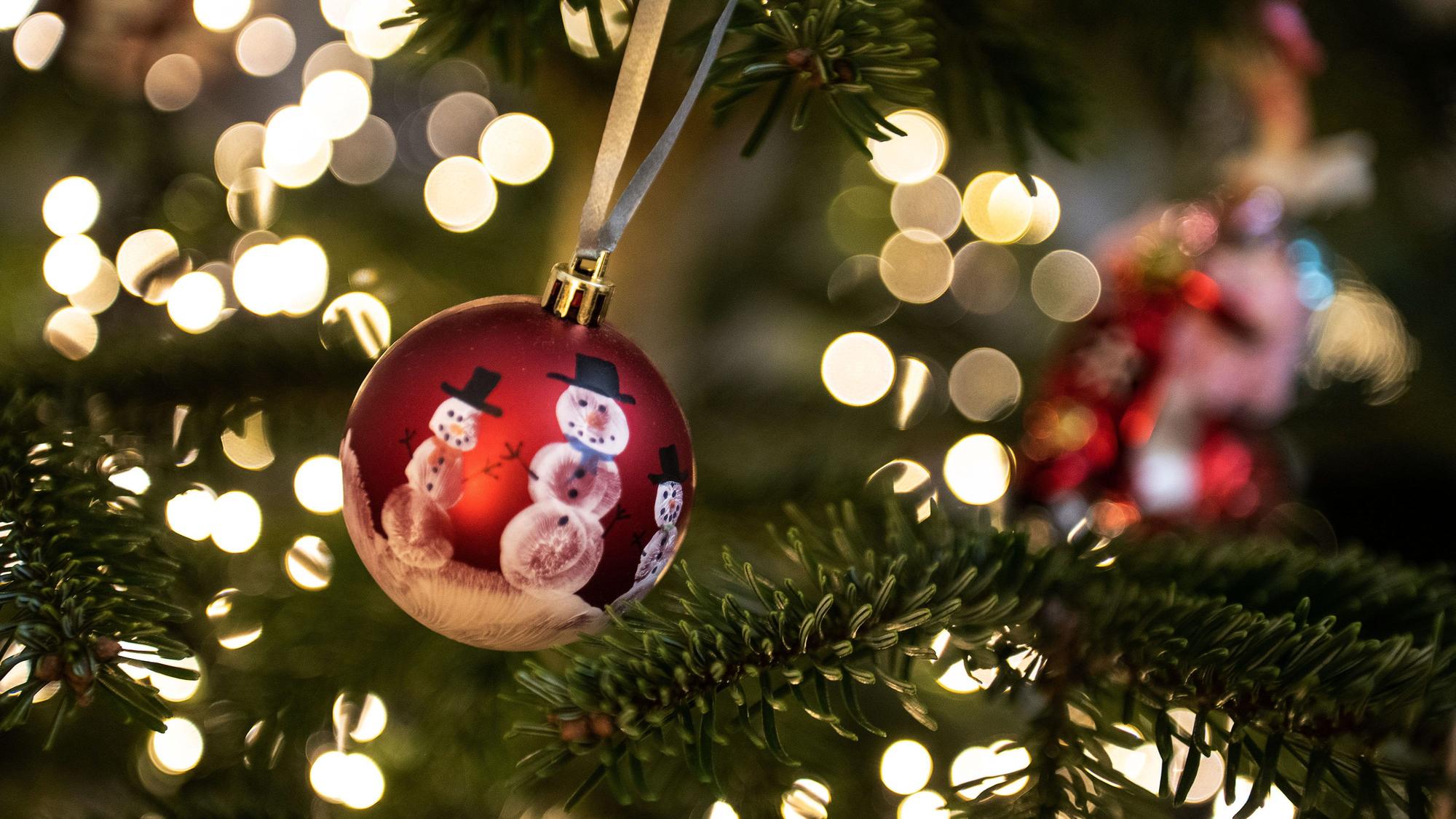 Eine Weihnachtskugel hängt an einem Weihnachtsbaum mit einer Lichterkette. (Symbolbild)
