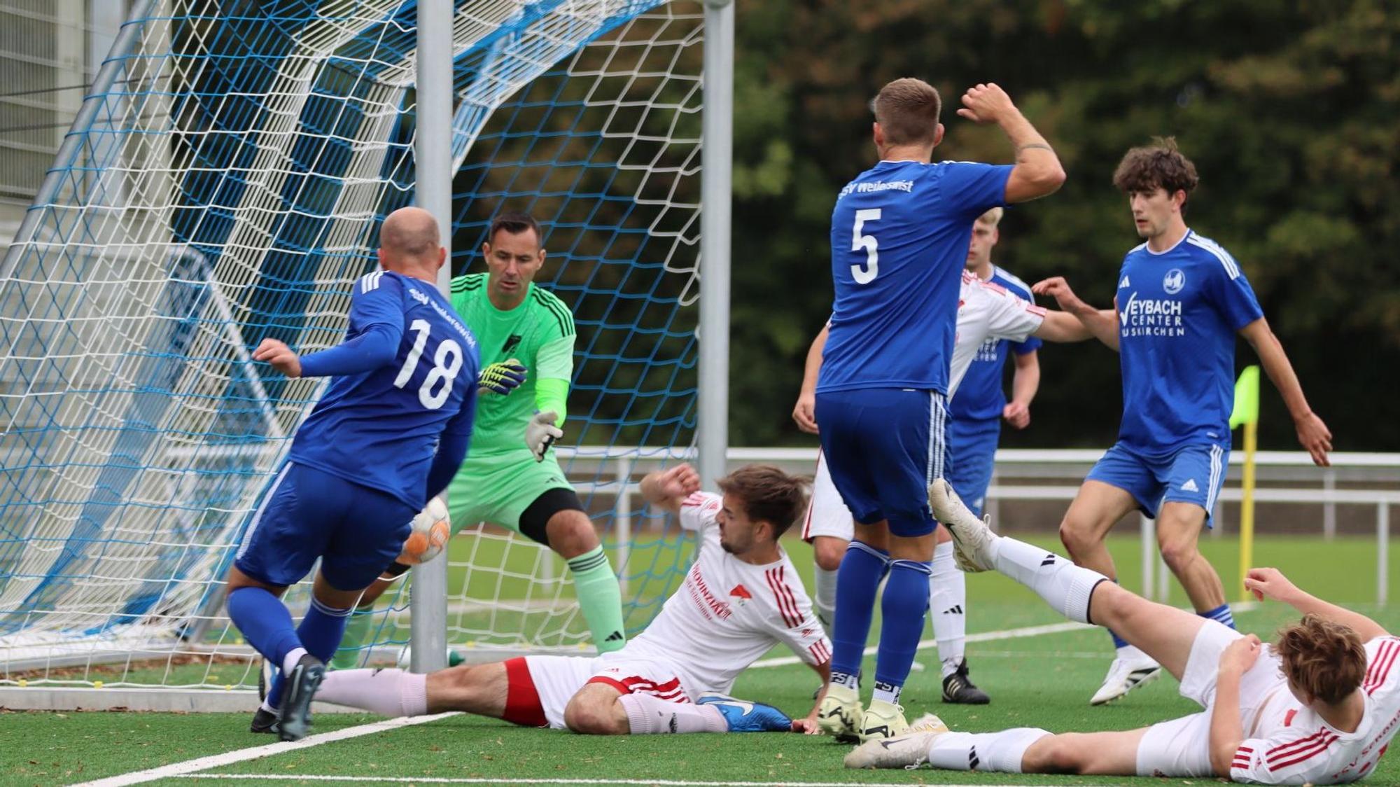 Das Bild zeigt zwei Spieler des TSV Schönau, die auf dem Boden liegen. Ein Spieler des SSV Weilerswist versucht, den Ball nach innen zu spielen.