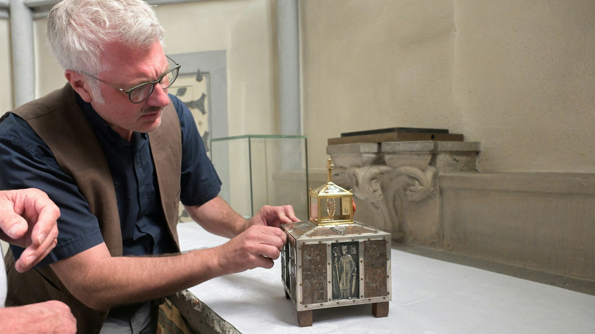 Ein weißhaariger Mann mit Brille und Schnauzbart versucht, ein kleines, silbern verziertes Kästchen zu öffnen.