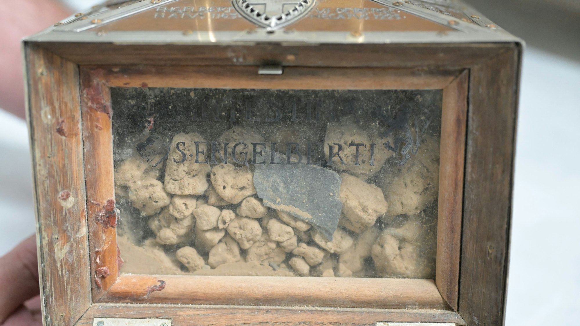 Ein kleines Kästchen. Hinter einer Glasscheibe sieht man unterschiedlich große gelb-graue Brocken. Auf der Scheibe steht: S. Engelbert.