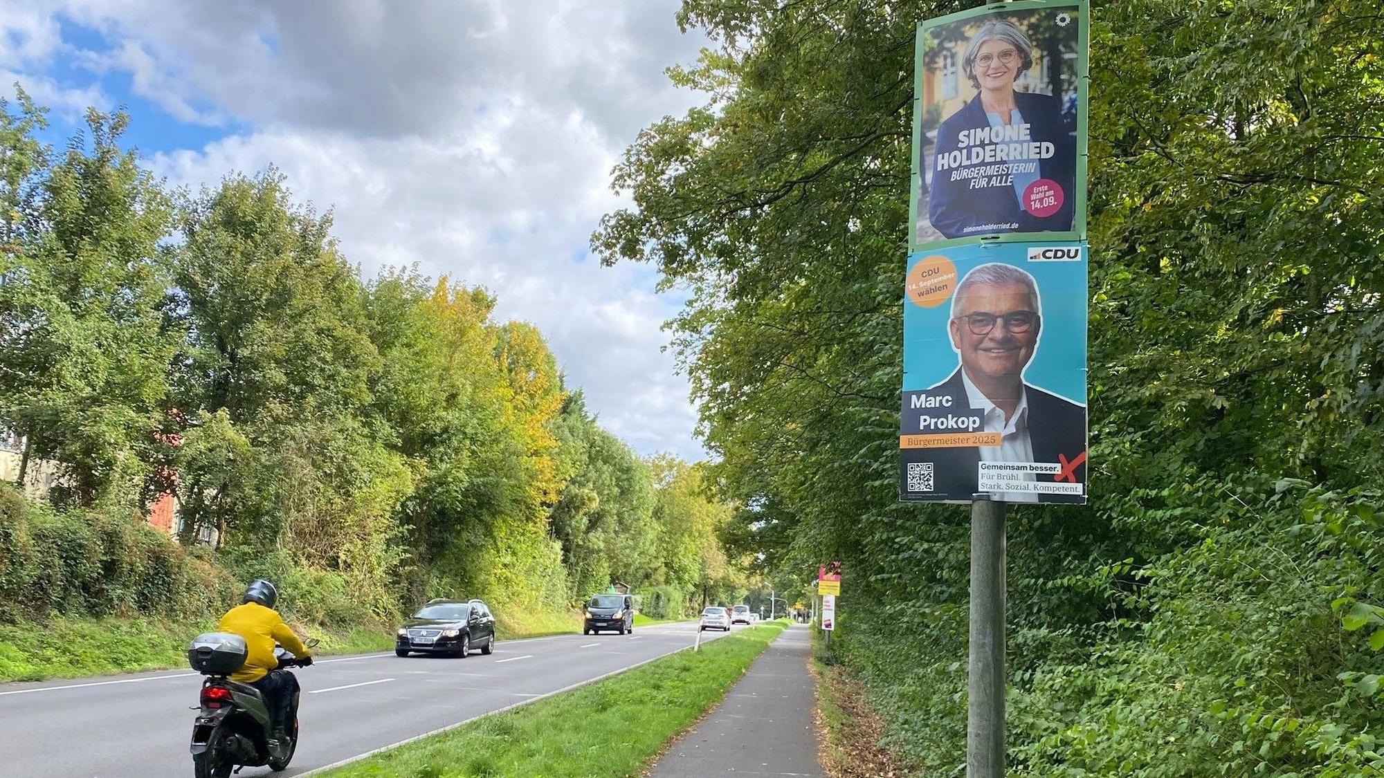 Zu sehen sind Wahlplakate der beiden Kandidaten und eine Straße.