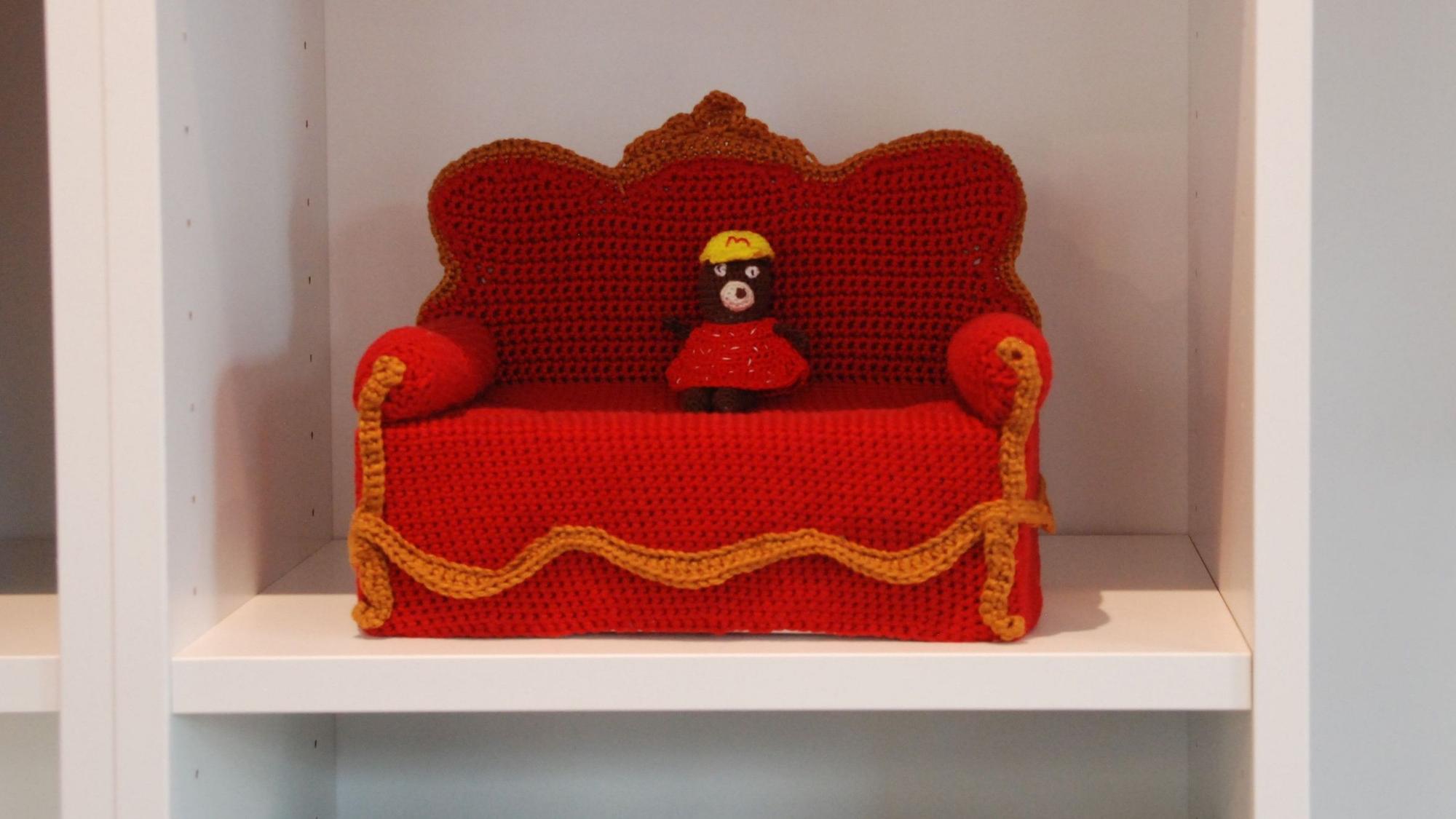 Im Regal der Buchhandlung steht ein aus rotem Garn gehäkeltes Miniatur-Sofa.