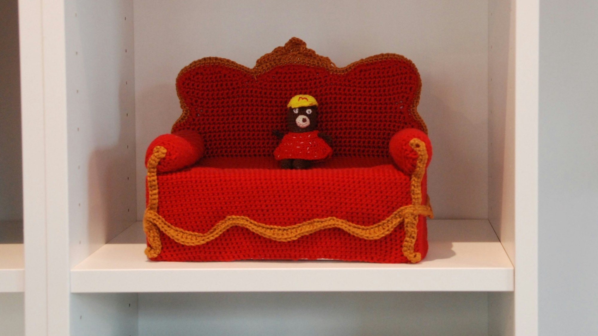 Im Regal der Buchhandlung steht ein aus rotem Garn gehäkeltes Miniatur-Sofa.