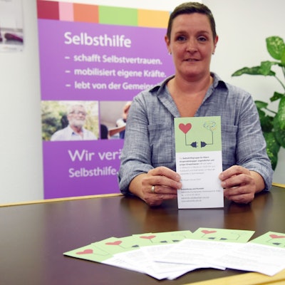 Eine Frau hält den Flyer einer neuen Selbsthilfegruppe in den Händen.