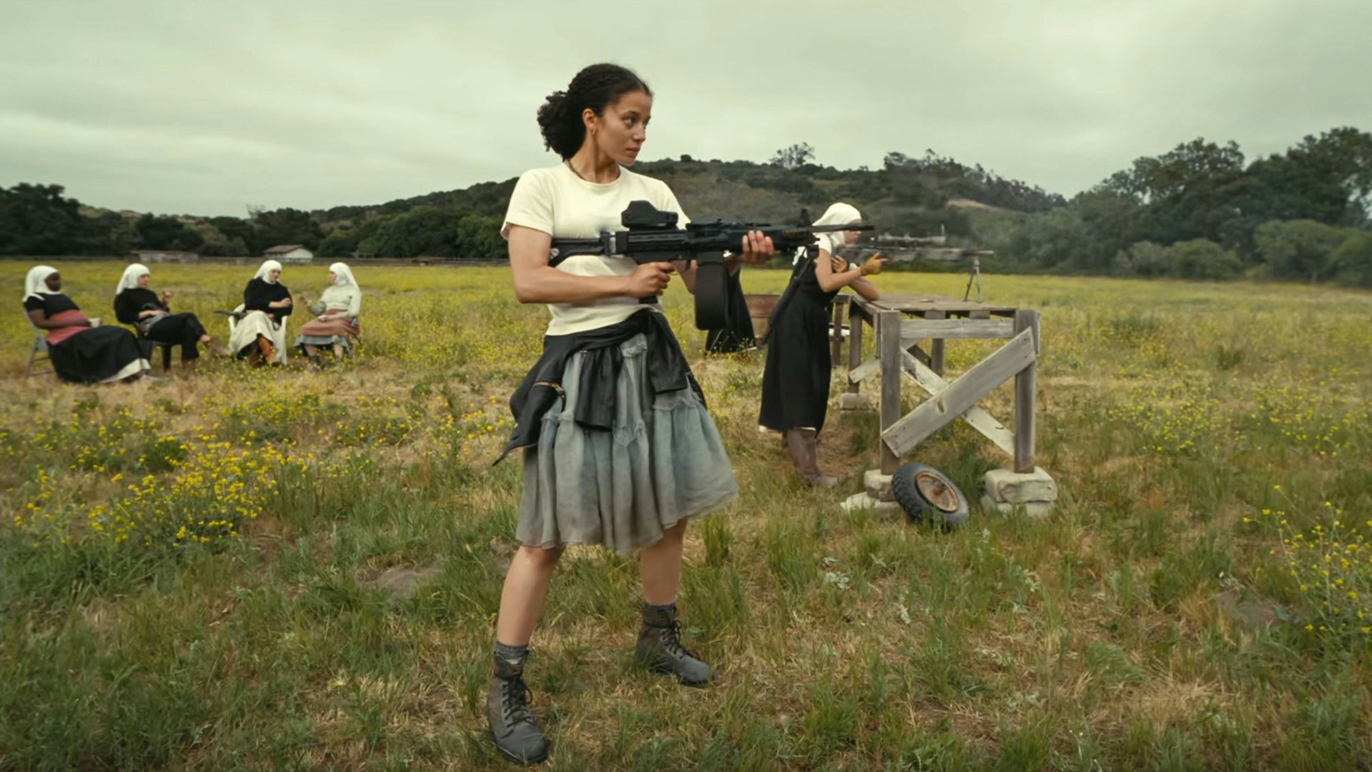 Chase Infiniti als Willa Ferguson übt sich zusammen mit einer Gruppe von Nonnen auf einer Wiese im Maschinengewehr-Schießen.