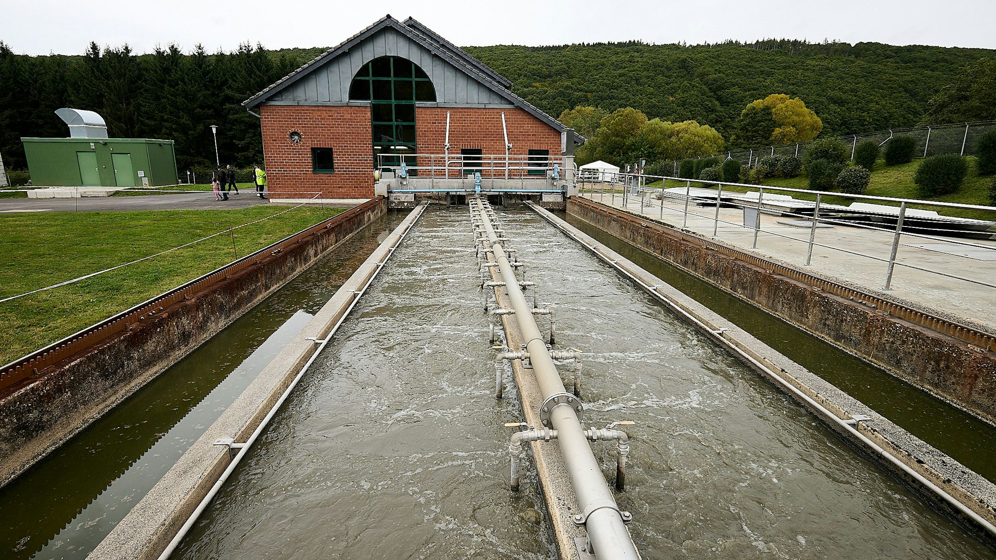 Im Hintergrund ist ein Gebäude der Kläranlage in Gemünd zu sehen, im Vordergrund ein Becken voller Wasser.