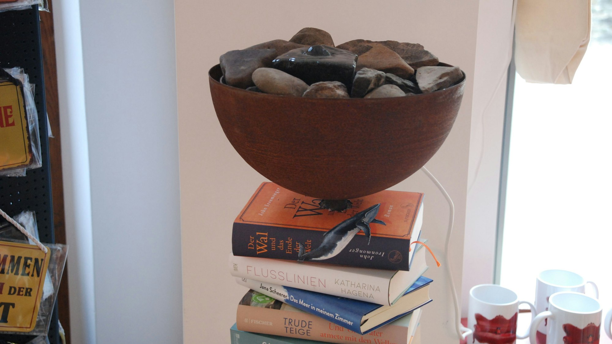 Auf einem Turm aus Büchern thront die mit Steinen gefüllte Schale eines Zimmerspringbrunnens.