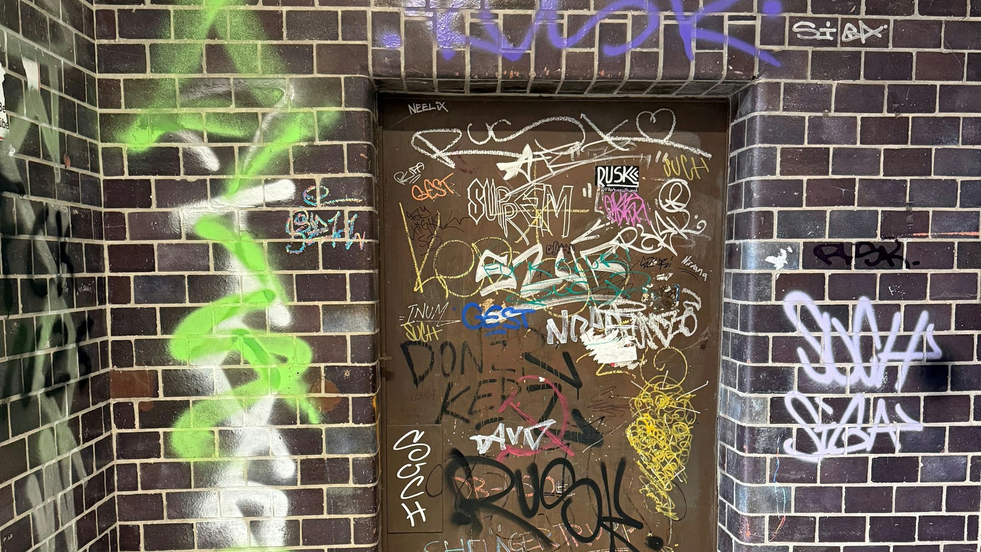 Eine beschmierte Wand und Tür mit verschiedenen Graffiti.