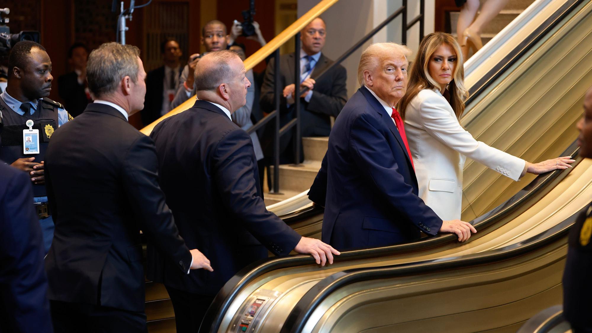 US-Präsident Donald Trump und First Lady Melania Trump schauen sich irritiert um, nachdem die Rolltreppe plötzlich stehen bleibt.