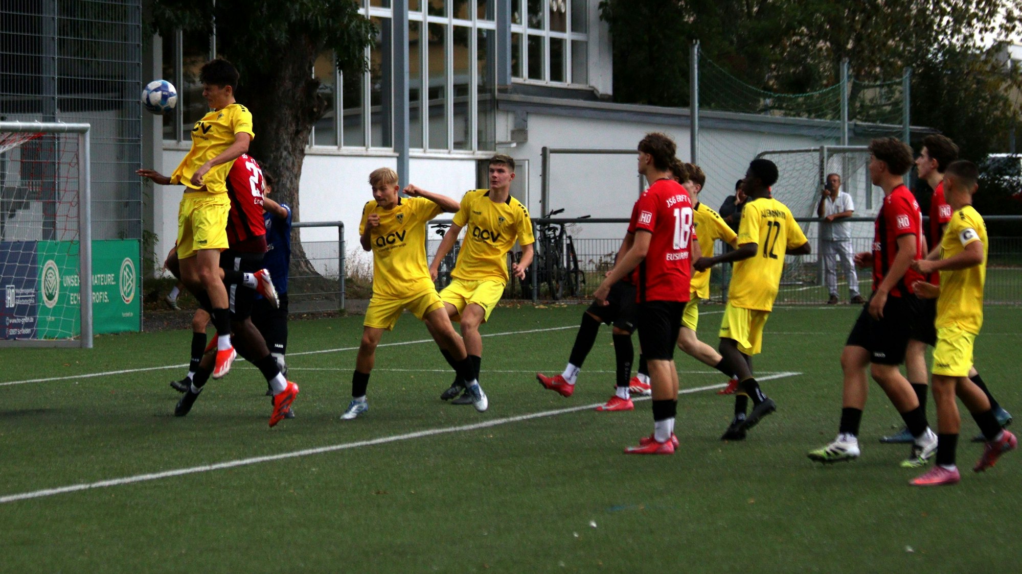 Ein Aachener Fußballer erreicht den Ball vor dem Gegenspieler der JSG Erft und dem gegnerischen Torwart per Kopf und erzielt ein Tor.