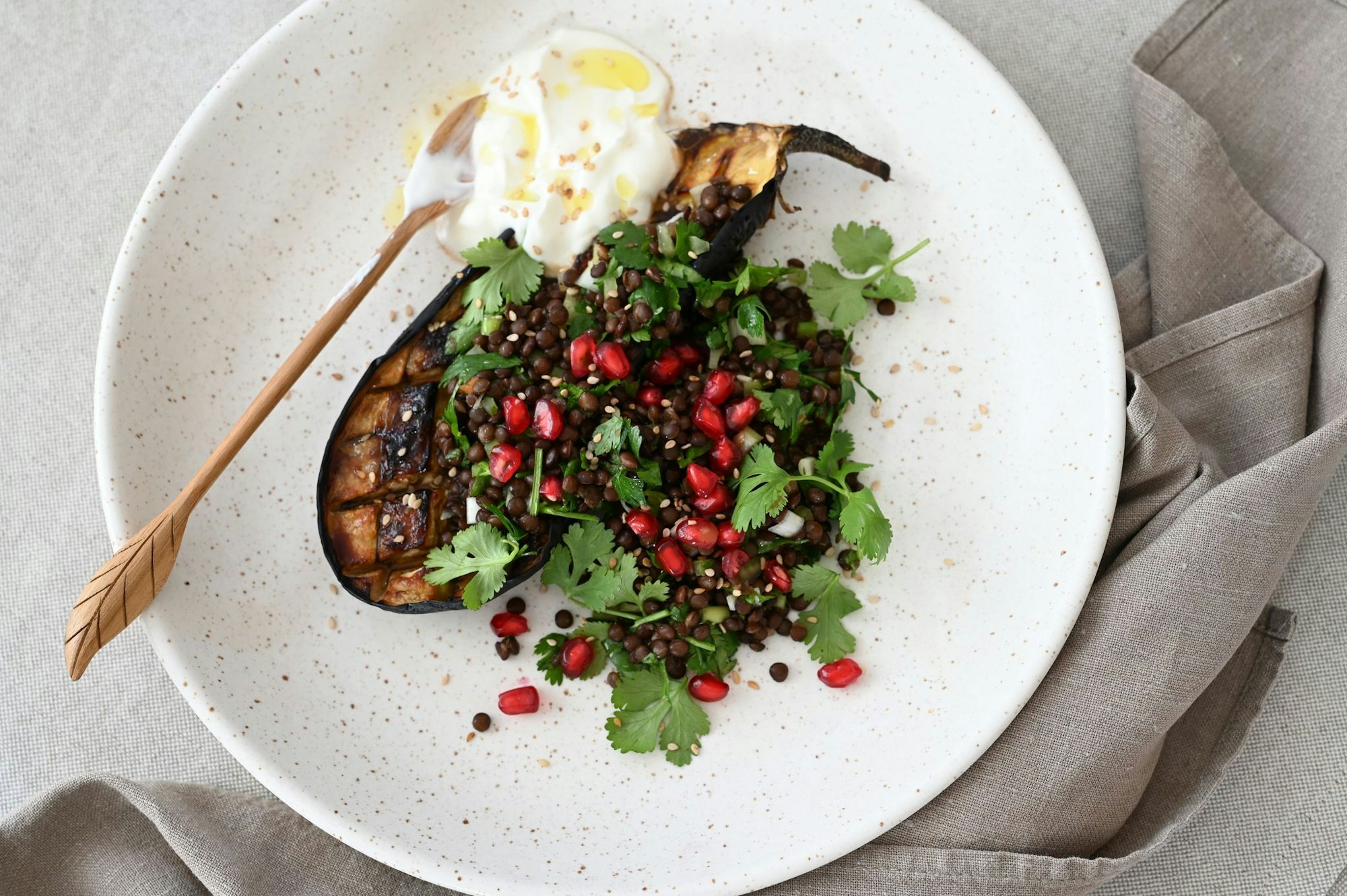 Ein Teller voller Kontraste und orientalischem Twist: Geschmorte Auberginen, getoppt mit Linsen-Kräuter-Salat, Granatapfelkernen und einem Klecks cremigem Joghurt.