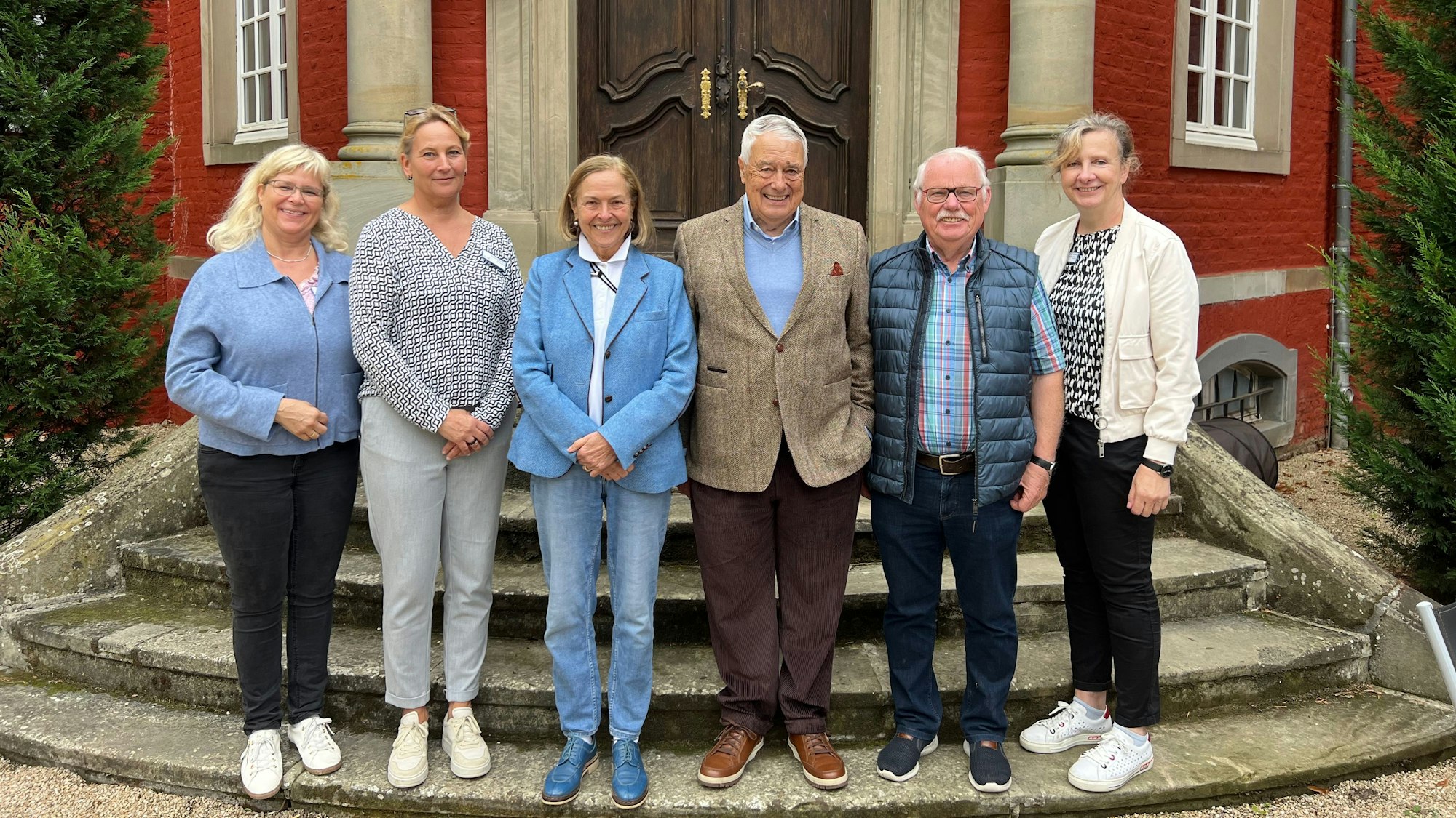 Menschen stehen vor der hölzernen Tür eines roten Schlosses.