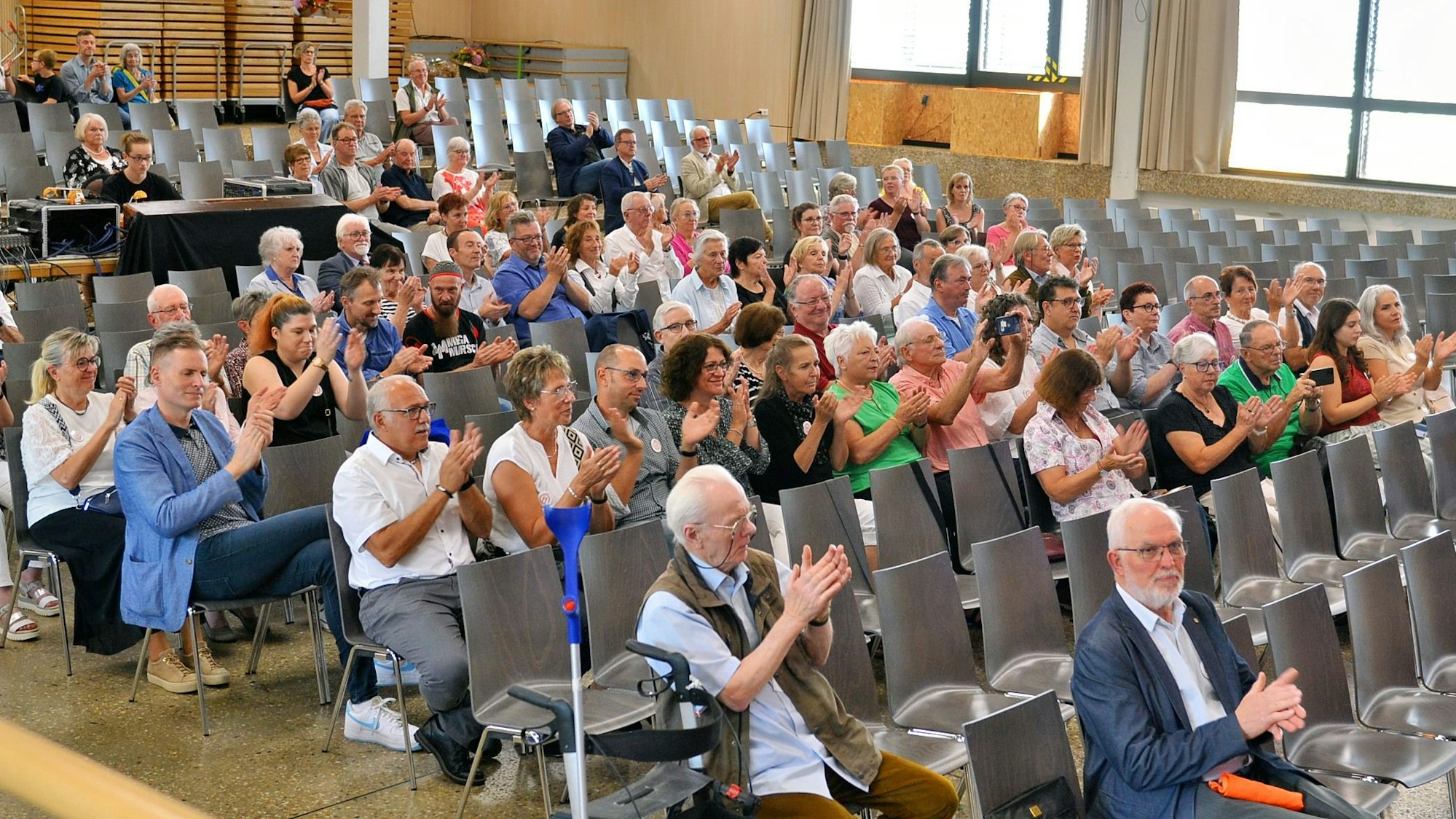 Menschen sitzen in Stuhlreihen in der Aula und klatschen Beifall.
