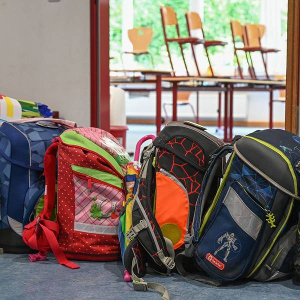 Viele bunte Schultornister stehen vor einem Klassenraum, in dem die Stühle hochgestellt sind.