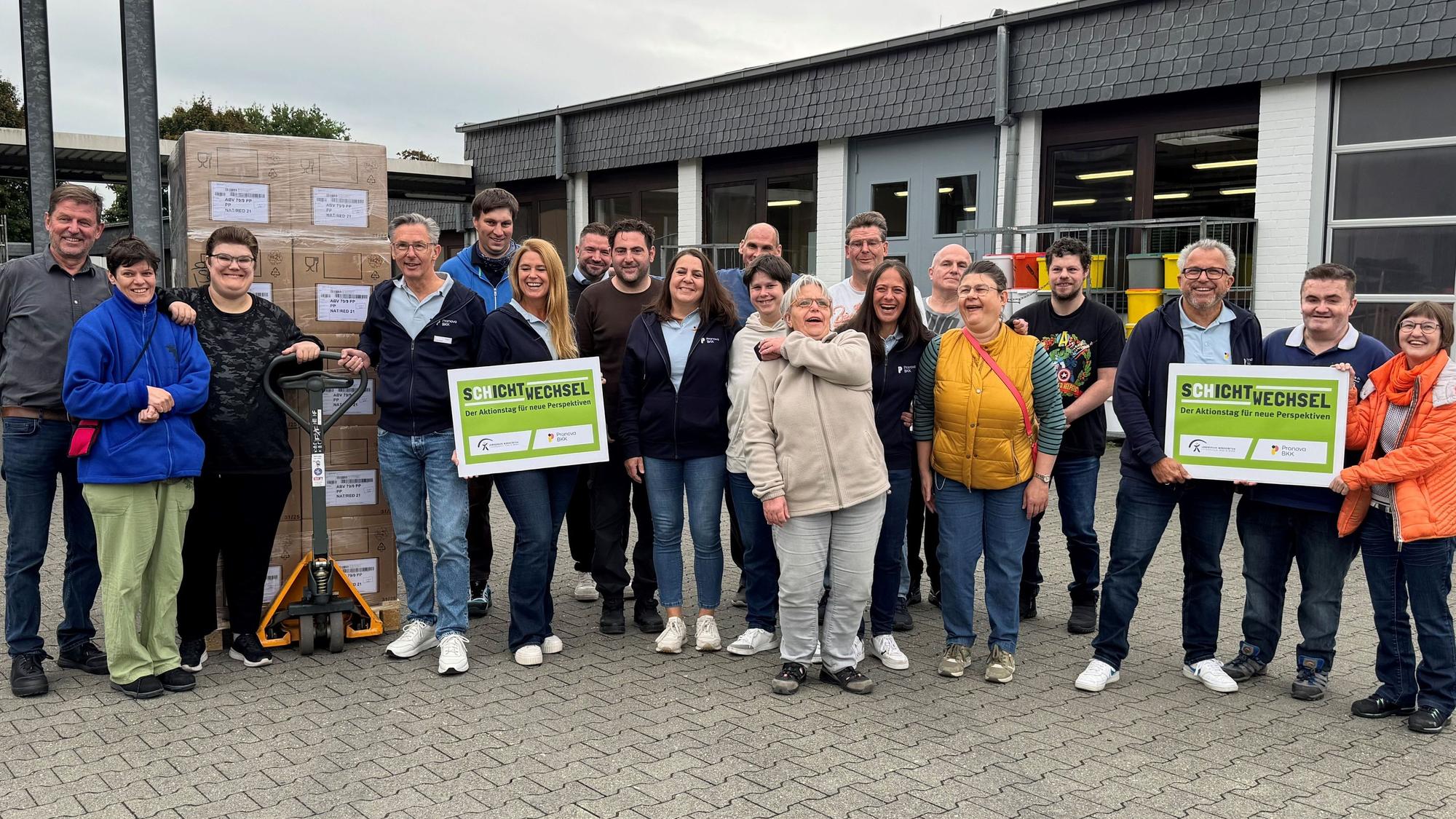 Menschen stehen auf dem Hof eines Betriebes mit Schildern in der Hand.