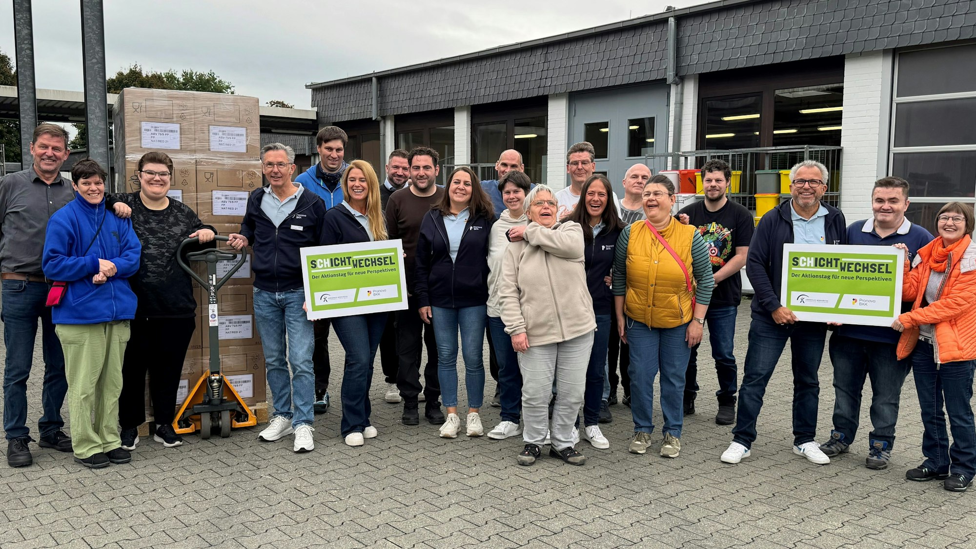 Menschen stehen auf dem Hof eines Betriebes mit Schildern in der Hand.