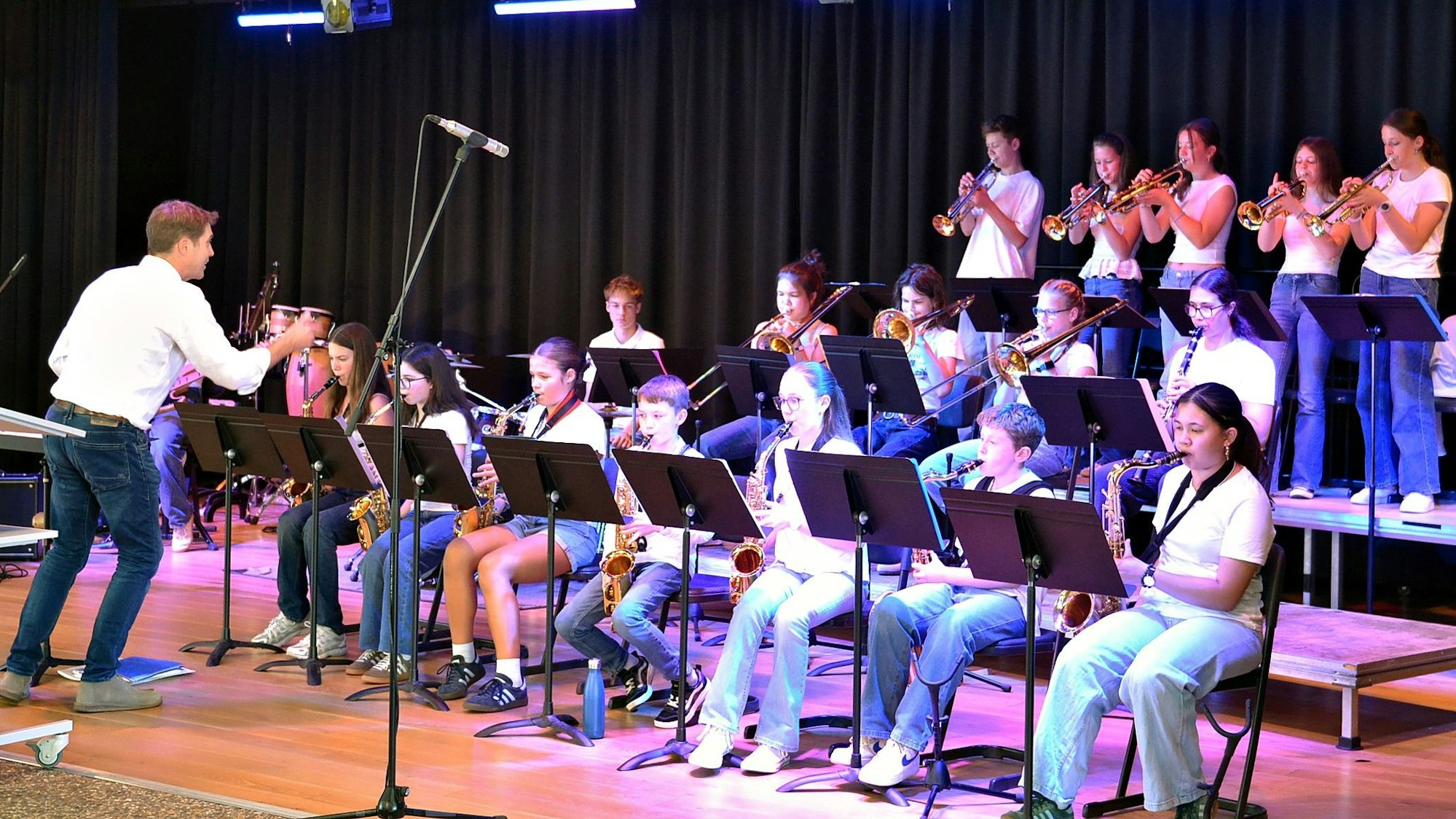 Ein Orchester mit jungen Musikern sitzt auf der Bühne, links agiert der Dirigent.