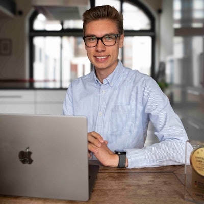 Das Bild zeigt David Schumacher am Küchentisch. Vor ihm steht ein Laptop und der gewonnene Preis.