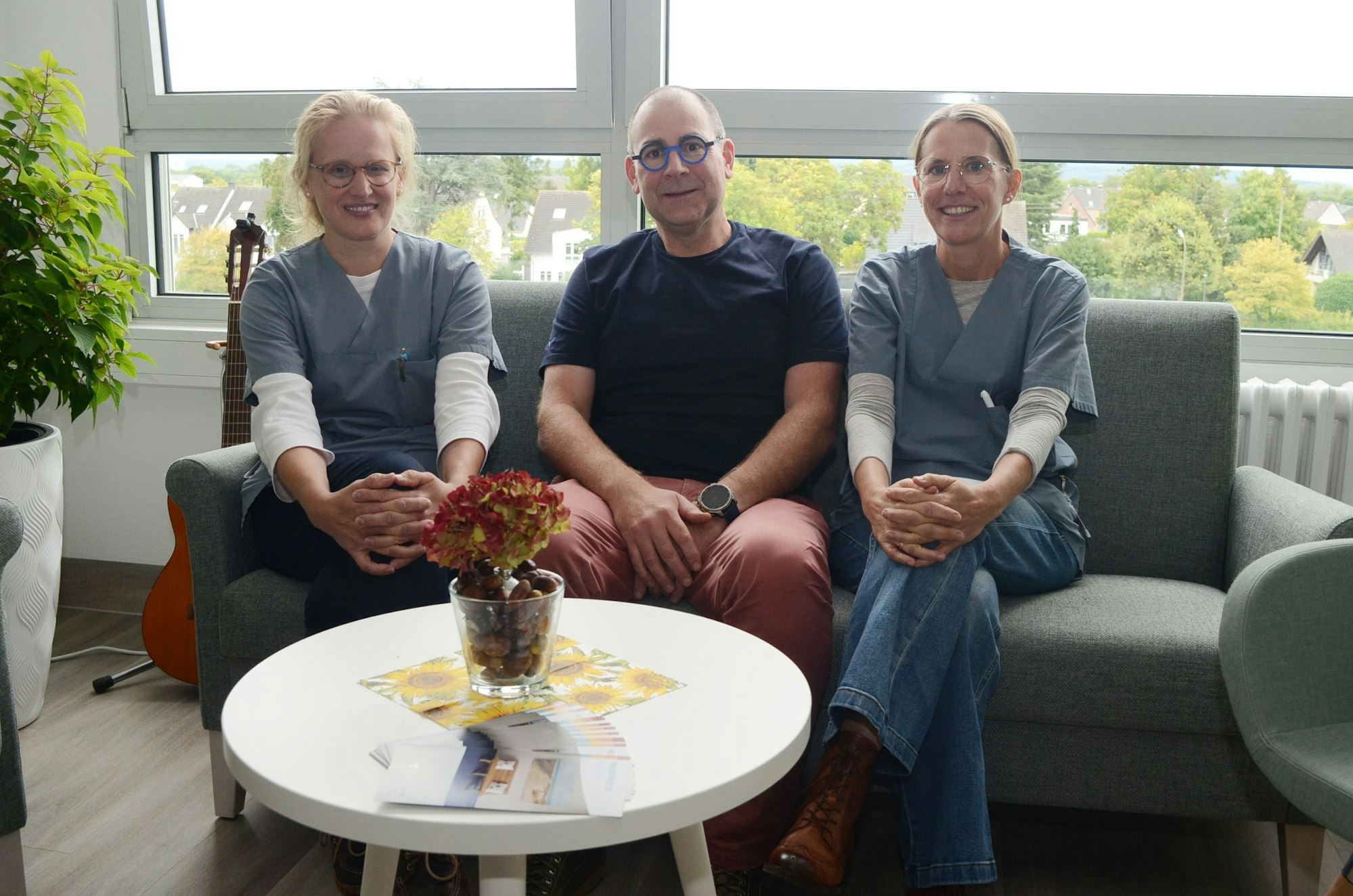 Zwei Frauen sitzen auf einem Sofa, zwischen ihnen ein Mann im dunklen T-Shirt.