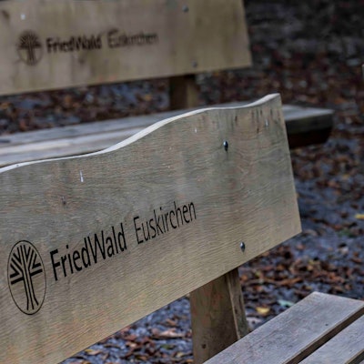 Das Bild zeigt zwei Holzbänke für Trauergäste. Sie tragen die Inschrift: Friedwald Euskirchen.