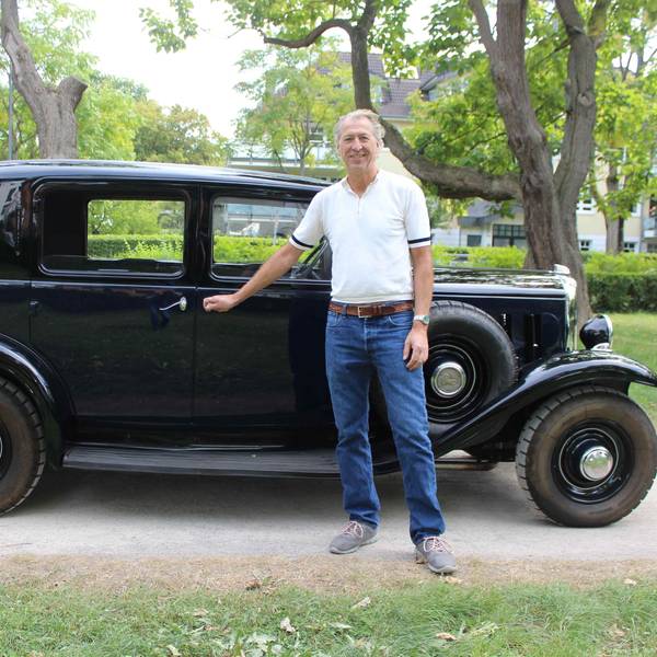 Ein Mann in blauer Jeans und weißem Shirt steht vor einem schwarzen Citroën Rosalie.