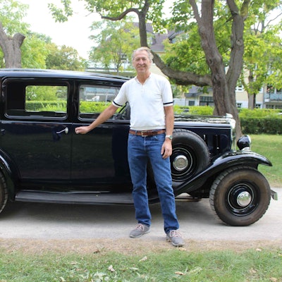 Ein Mann in blauer Jeans und weißem Shirt steht vor einem schwarzen Citroën Rosalie.