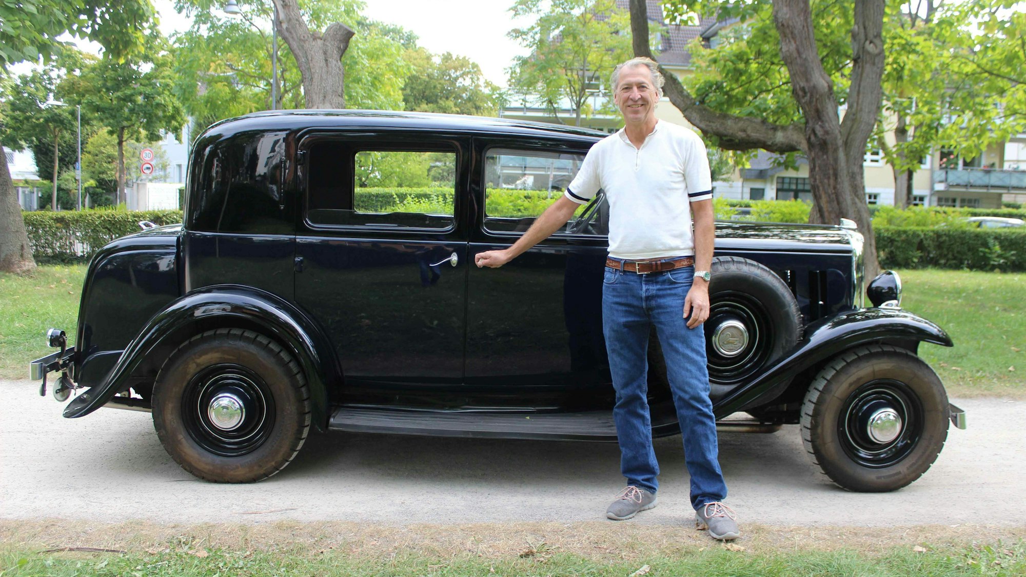 Ein Mann in blauer Jeans und weißem Shirt steht vor einem schwarzen Citroën Rosalie.