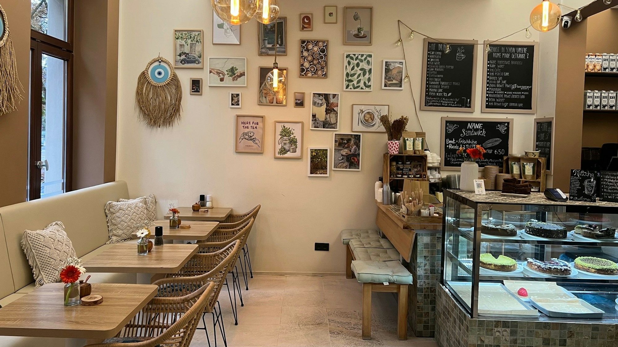 Ein Blick ins Café Nane, mit Stühlen und Tischen, Bildern an den Wänden und einer Theke mit Kuchen.