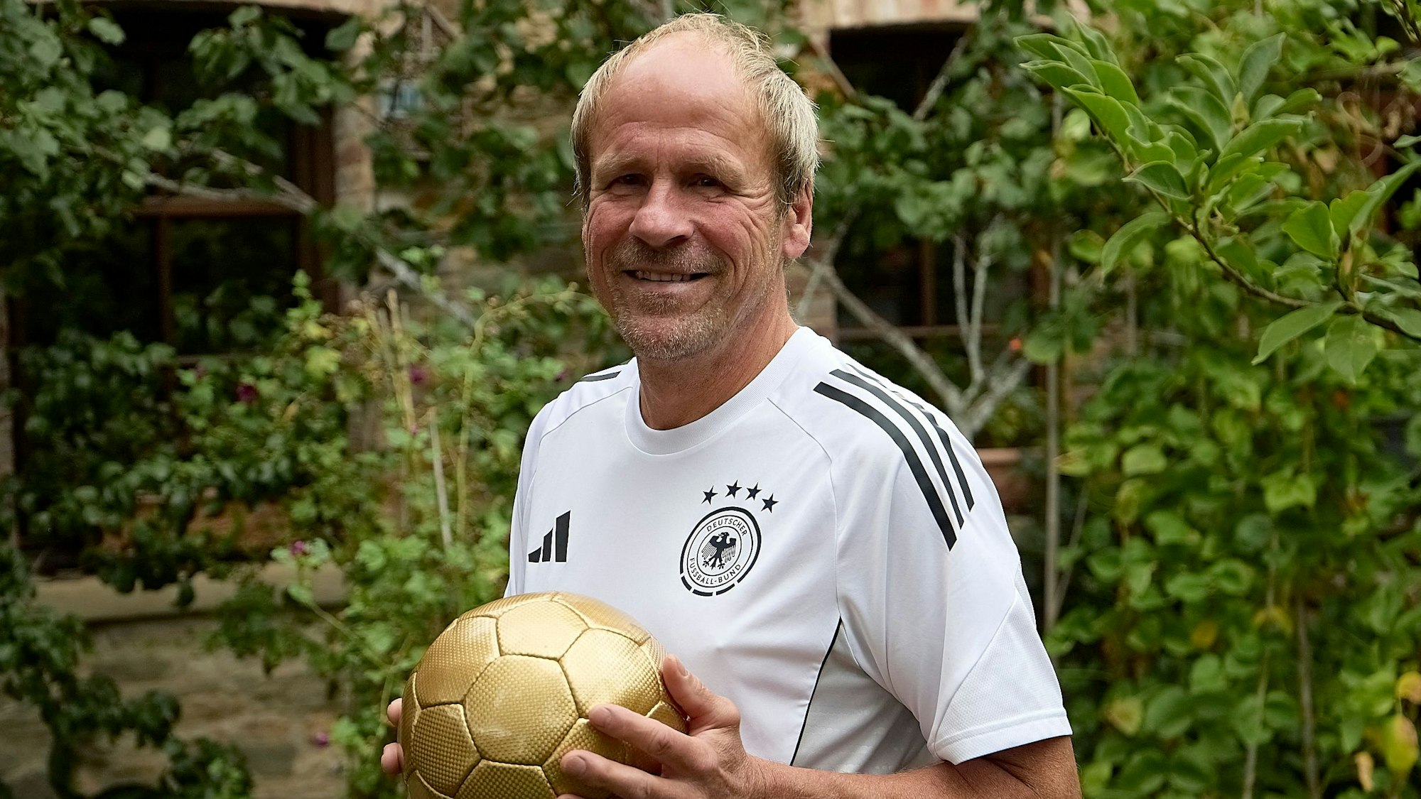Peter Siebert trägt ein weißes Fußballtrikot und hält einen goldenen Fußball in Händen.