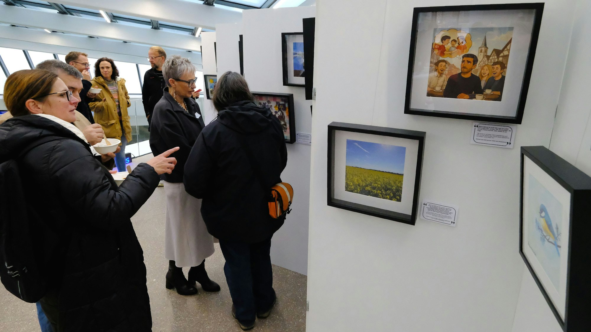 Eine Gruppe von Menschen steht vor einer Ausstellungswand, auf der mehrere gerahmte Bilder hängen.