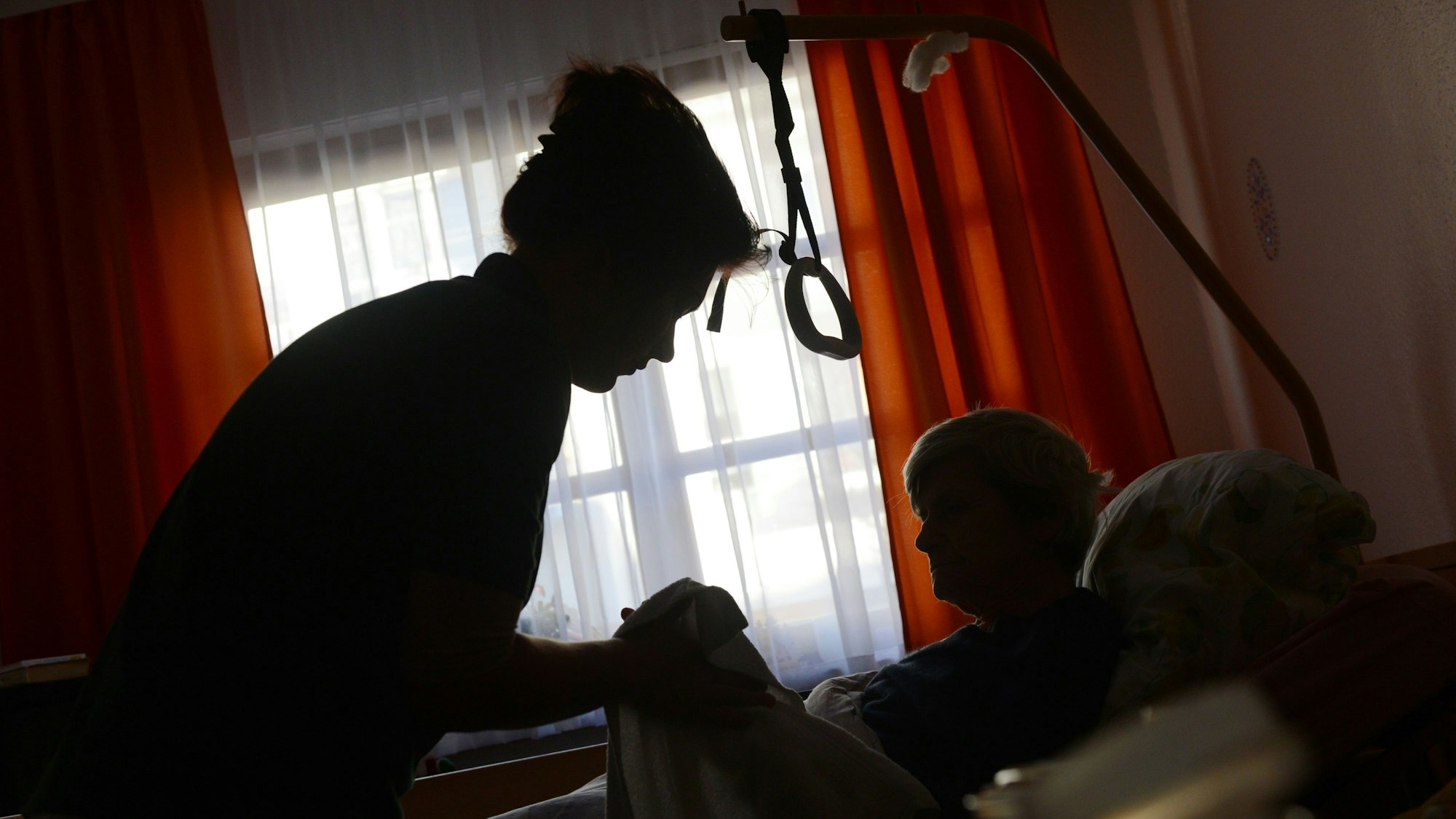 Eine Person kümmert sich um einen Menschen, der im Bett liegt