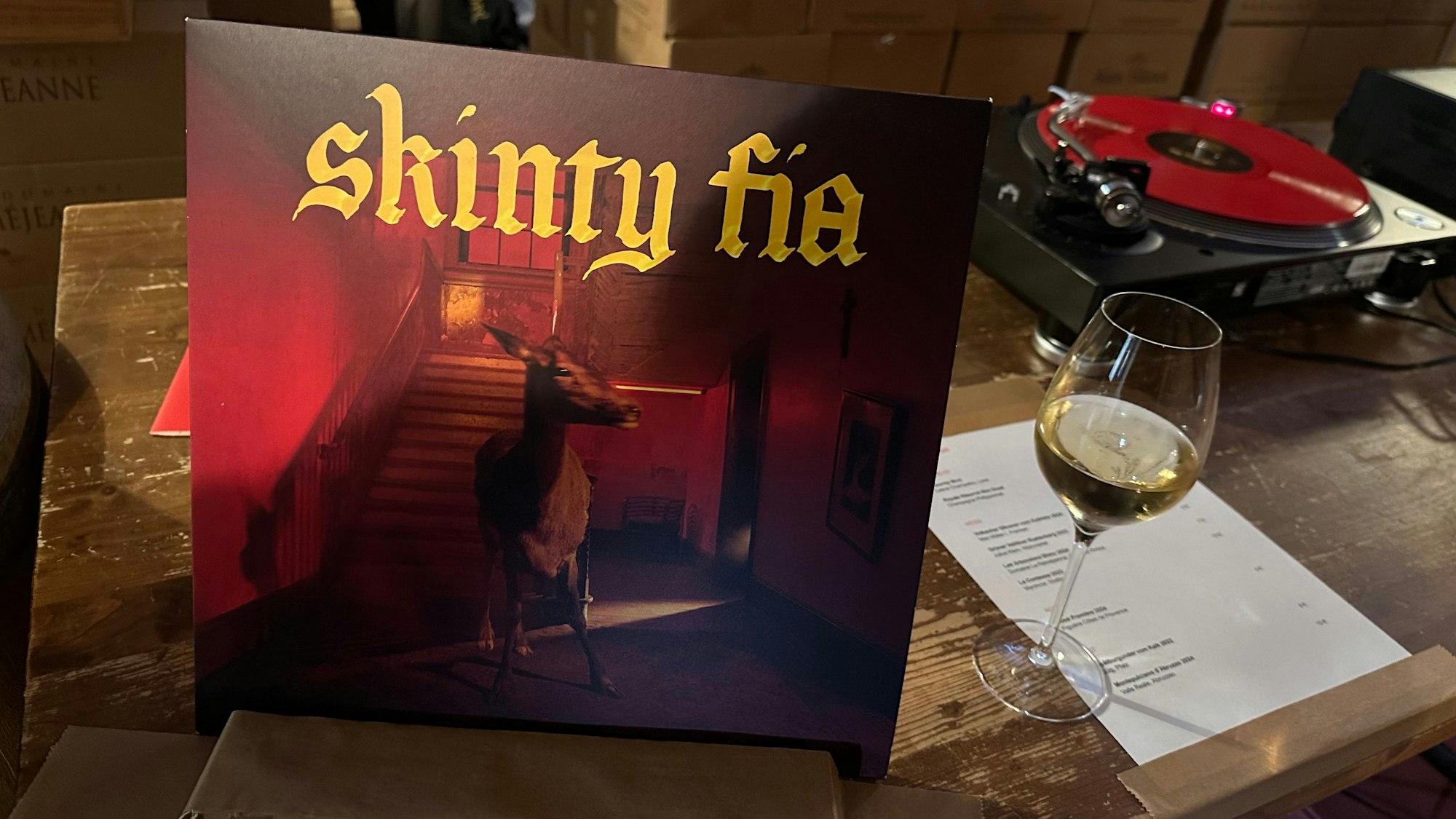 Das Bild zeigt einen Plattenspieler, eine Vinyl und ein Weinglas in der Lagerhalle.