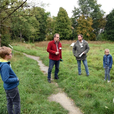 Blick auf zwei Männer, die einer Gruppe etwas erklären.
