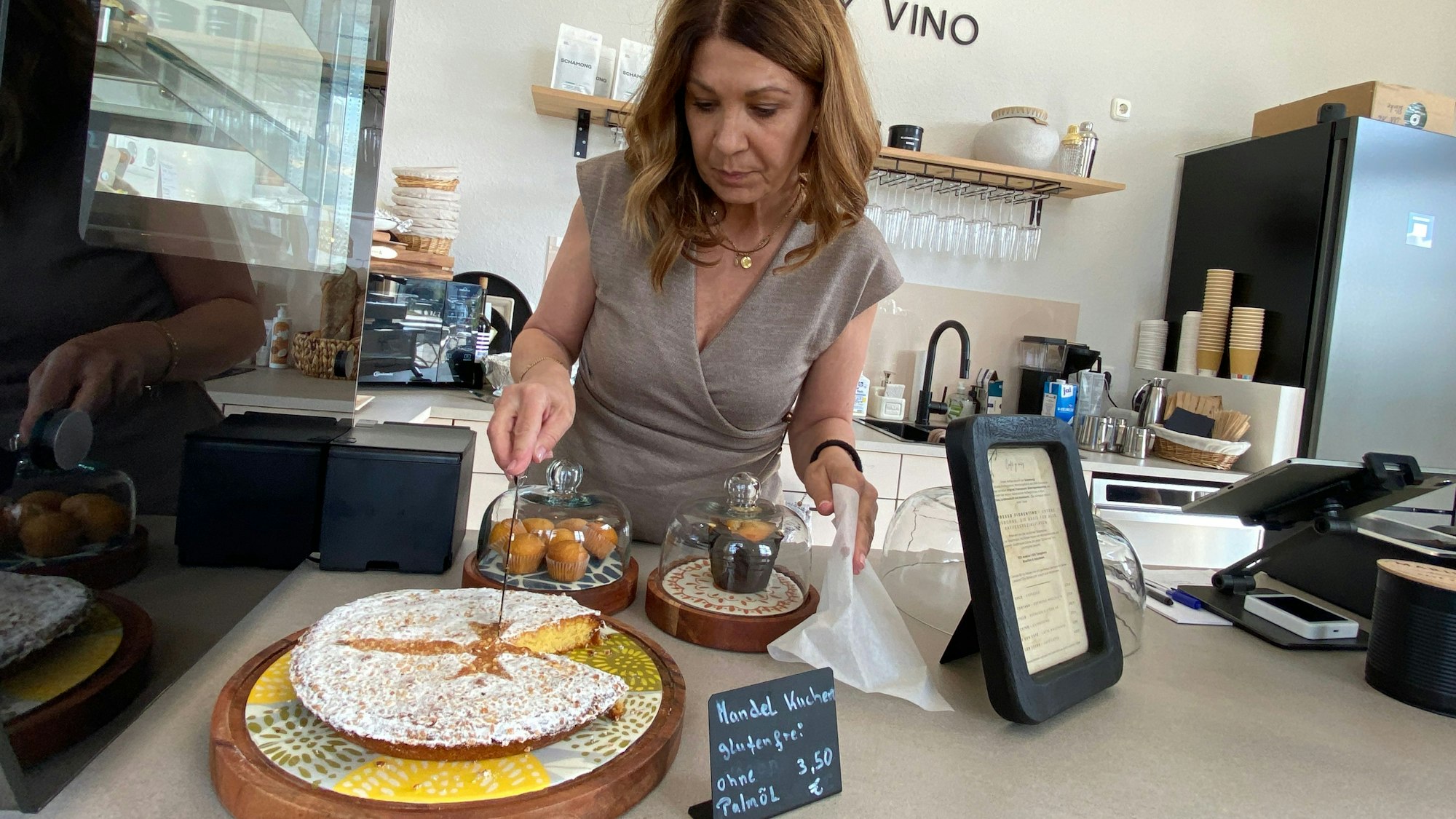 Eine Frau steht in einem Café an der Theke und schneidet einen Kuchen in Stücke.