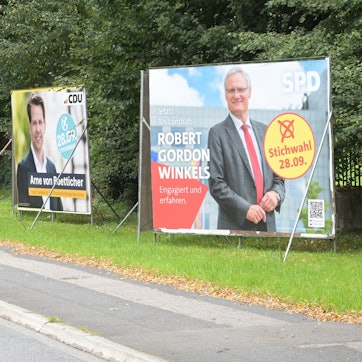 Wahlplakate zur Stichwahl der Kommunalwahl 2025 stehen an der Overather Straße in Bergisch Gladbach-Bensberg.