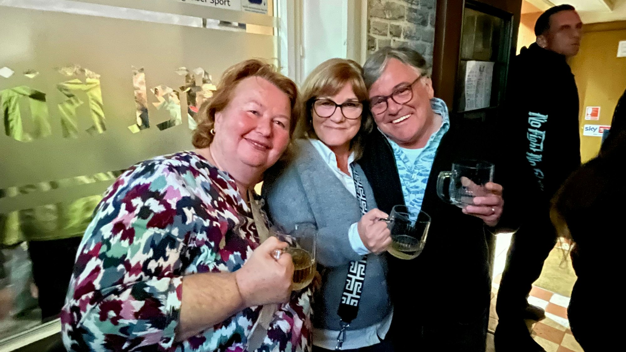 Zu sehen sind zwei Frauen und ein Mann mit Bechergläsern in der Hand.