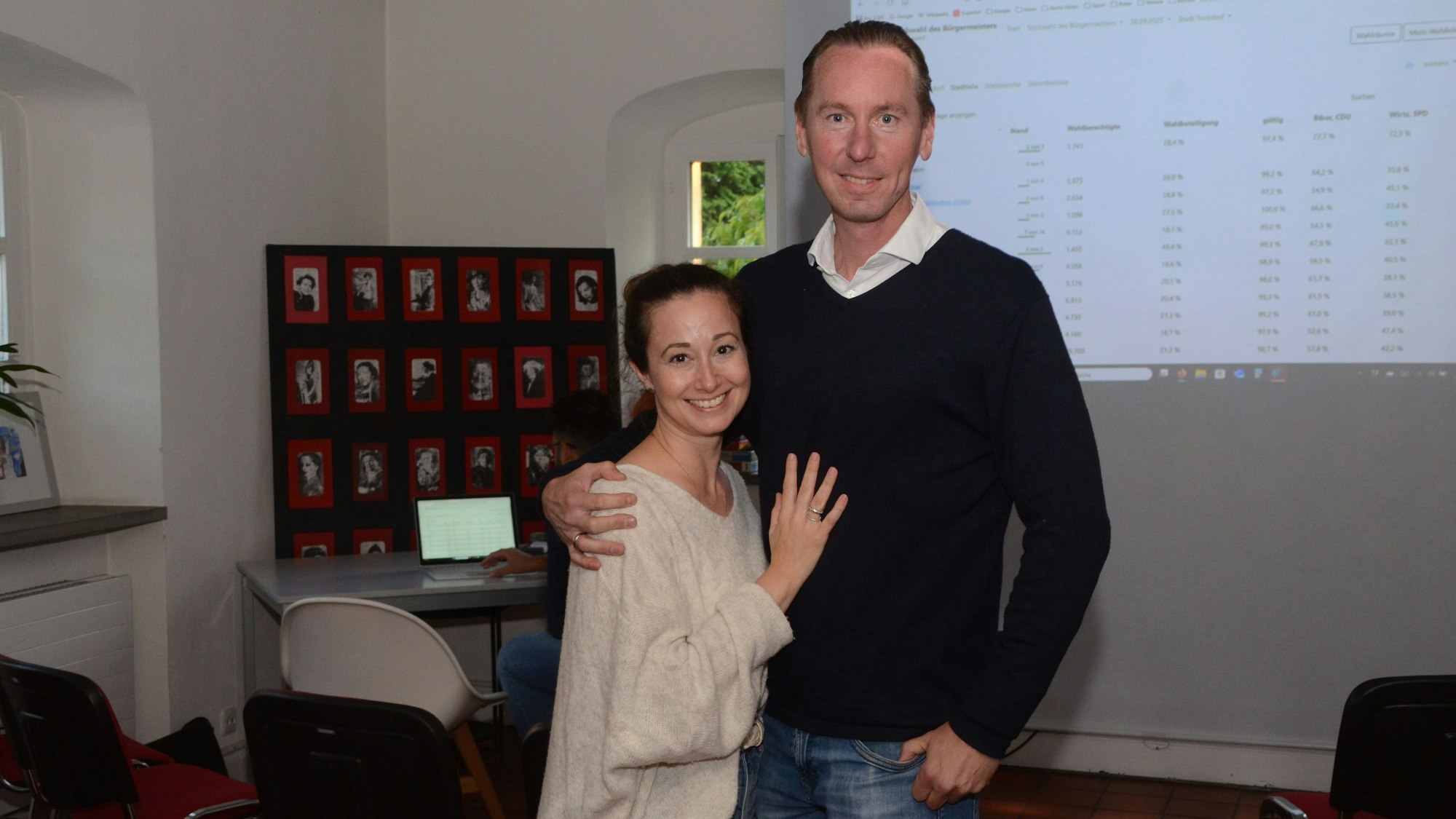 Ein Mann und eine Frau. Hinter ihnen werden Wahlergebnisse auf die Wand projiziert.