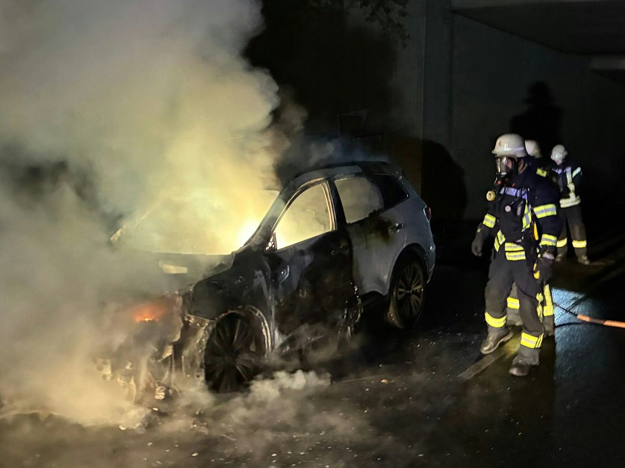 Das Bild zeigt zwei Feuerwehrleute an einem brennenden Auto.