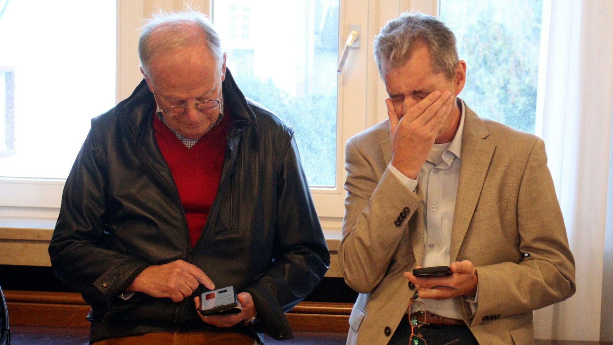 Zwei CDU-Mitglieder verfolgen die Zwischenergebnisse auf ihren Handys. Einer streicht sich mit der Hand durchs Gesicht.