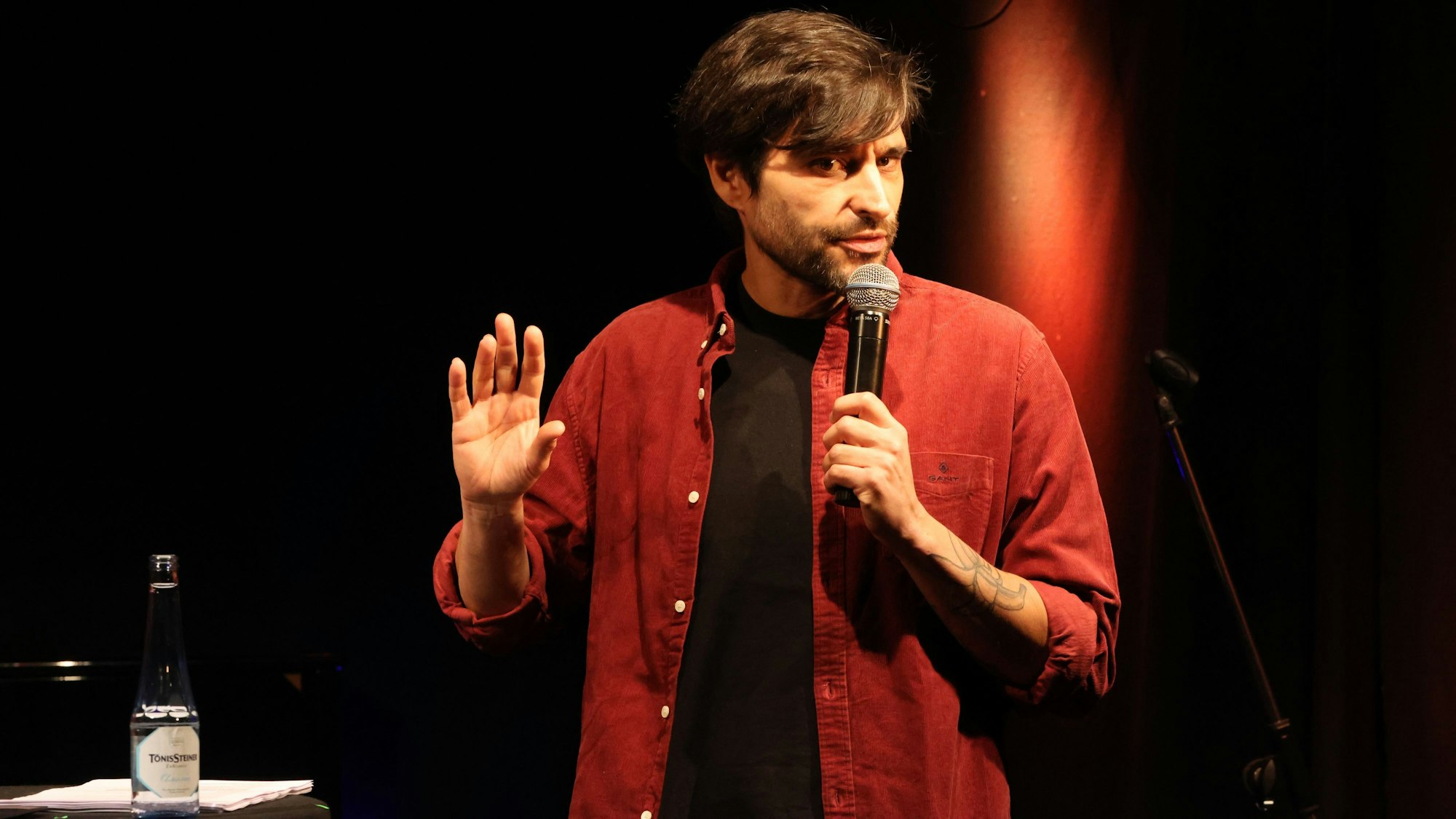 Nektarios Vlachopoulos steht mit Mikrofon auf der Bühne.